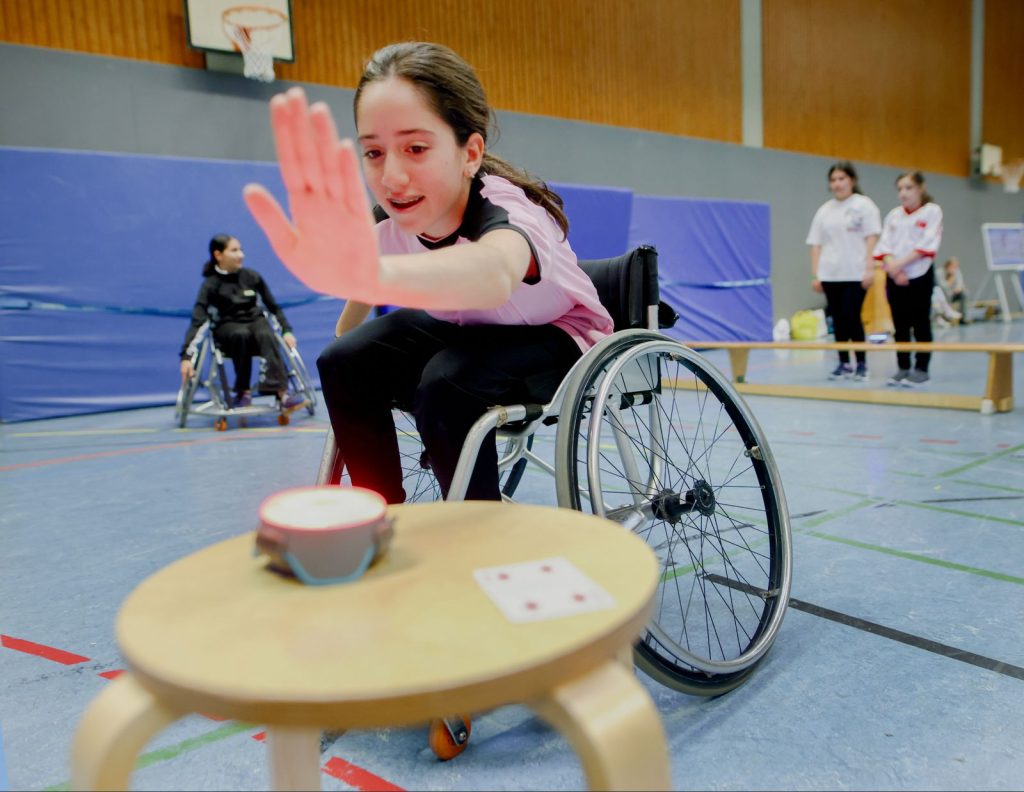 Ein Mädchen im Rollstuhl in einer Sporthalle voll in Aktion!